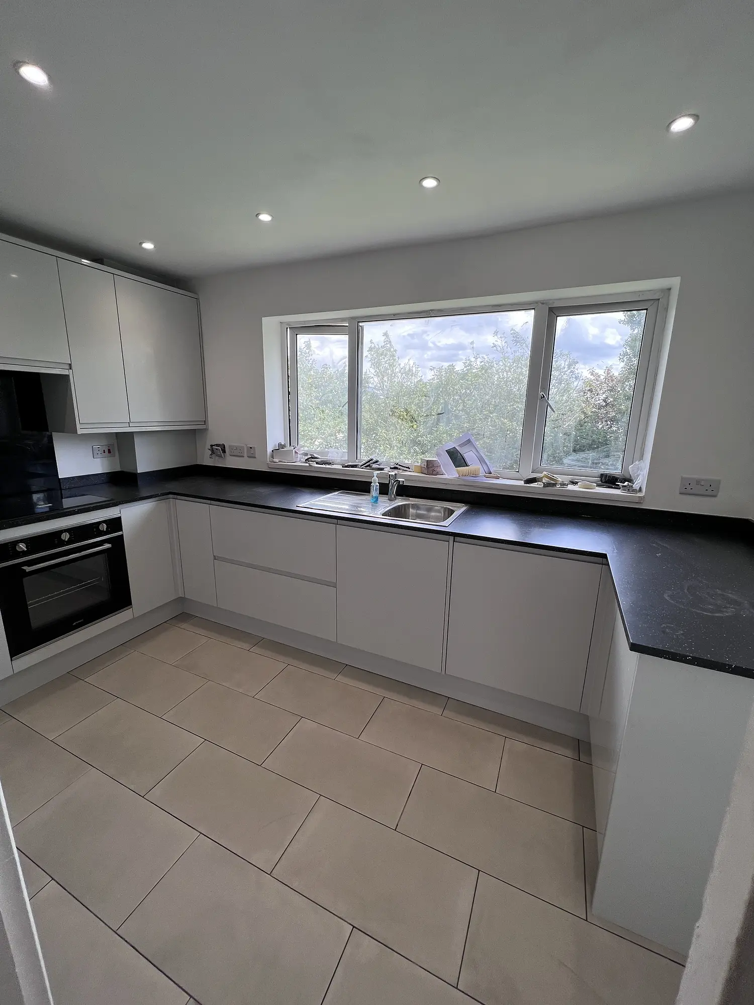 Minimal pale grey handleless kitchen with black worktops and wide garden window
