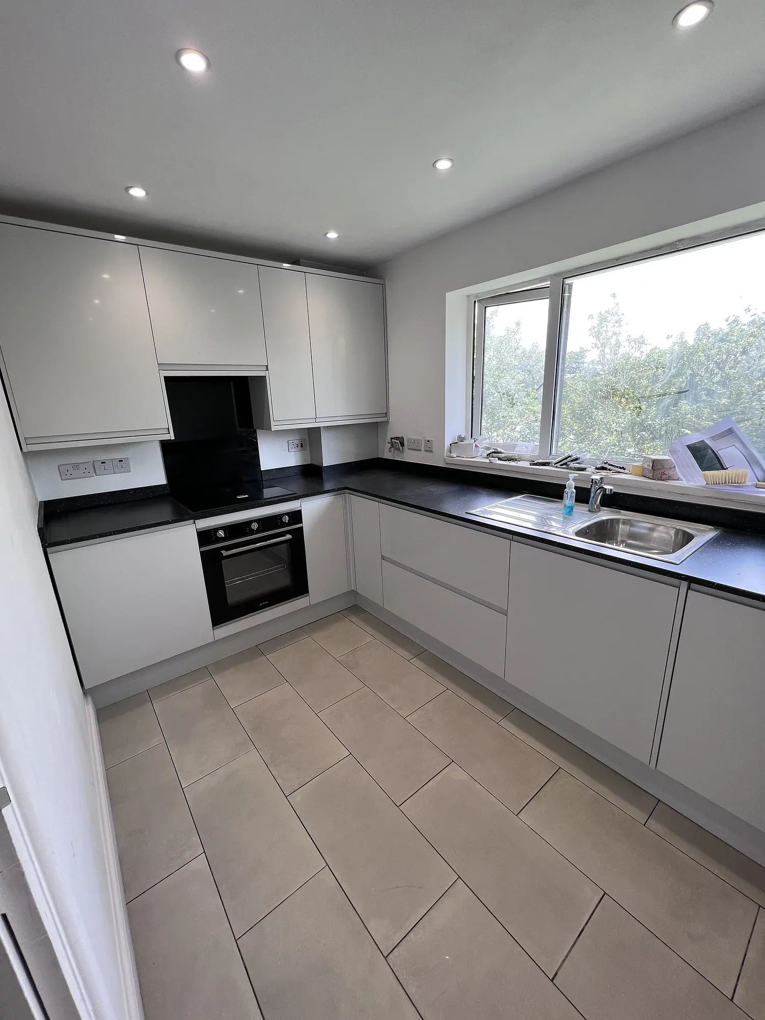 Contemporary white kitchen with black worktop, integrated oven and large window